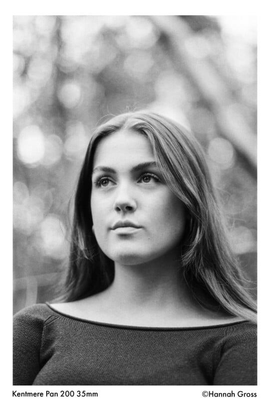 Black and white portrait of a young woman with long hair, looking slightly upward. She is wearing a dark top, with a softly blurred, nature-inspired background. The photo credits and film details are visible at the bottom.