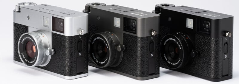 Three Fujifilm compact cameras are lined up side by side, each in a different finish: silver, dark gray, and black. All have a textured grip, lens, and a classic rangefinder-style design.
