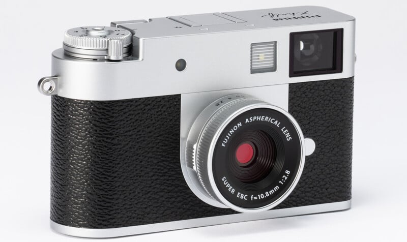 A vintage-style silver and black camera with a textured grip, prominent lens labeled "FUJINON ASPHERICAL LENS," and viewfinder, isolated on a white background.