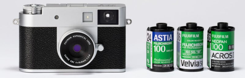 A silver and black film camera sits next to three rolls of Fujifilm film, labeled Astia 100F, Fujichrome Velvia 100, and Neopan 100 Acros, against a plain white background.