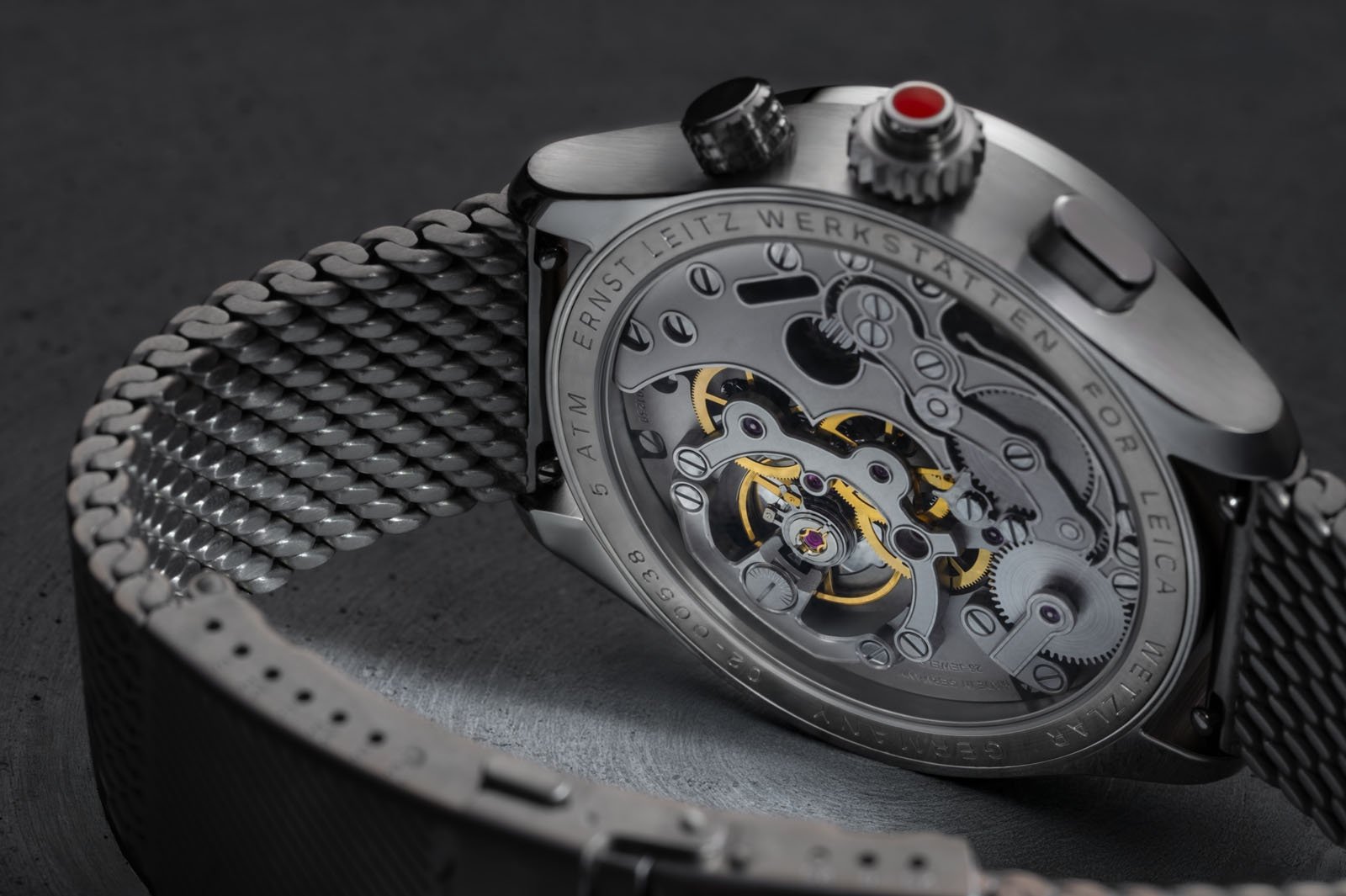 Close-up of the back of a luxury wristwatch with a metal mesh strap, showcasing its intricate mechanical movement and engraved details through a transparent case back.