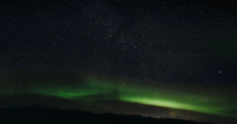 The night sky filled with stars and faint green aurora lights glowing above a dark, silhouetted landscape.