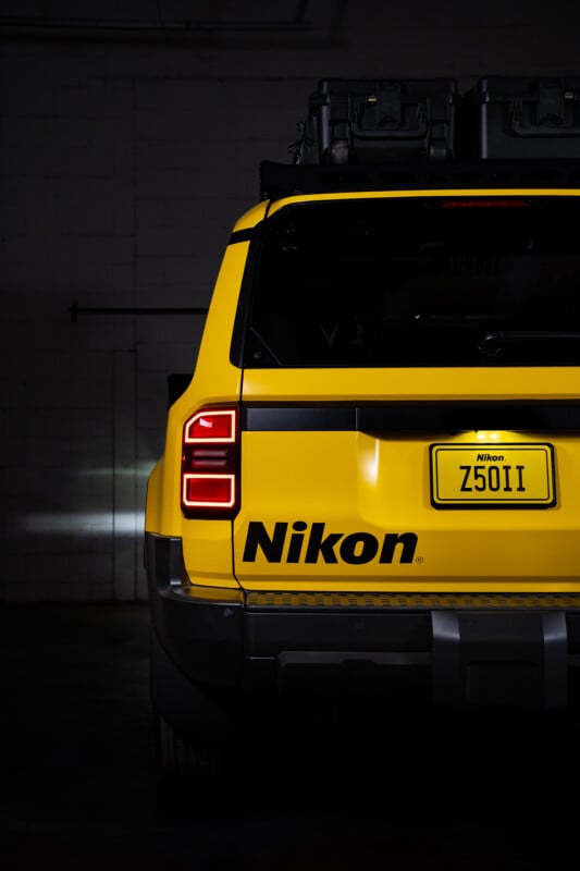 A yellow SUV with the Nikon logo and a custom license plate reading "Z50II" is parked indoors. The rear taillight is illuminated, and camera gear is mounted on the roof.