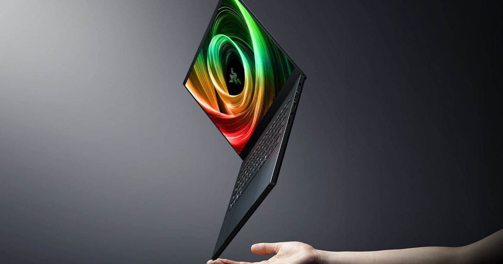 A thin, open laptop with a colorful spiral display hovers above an outstretched hand against a dark, gradient background.