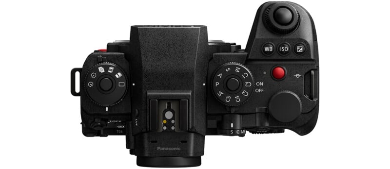 Top-down view of a black Panasonic camera showing control dials, buttons, and the hot shoe mount. Visible controls include ISO, white balance, mode dial, shutter button, and a red video record button.