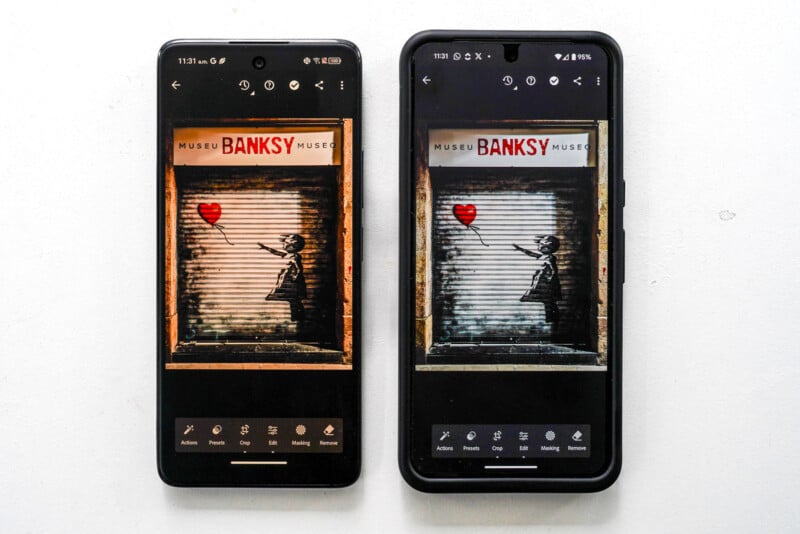 Two smartphones displaying the same image of Banksy's "Girl with Balloon" art, shown on museum shutters. The phones are side by side on a white surface, each with different color tones.