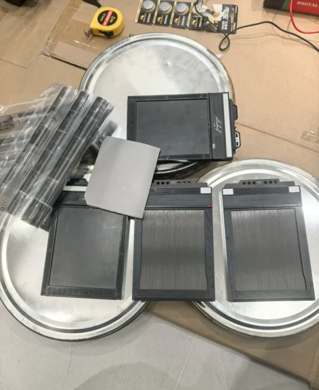 Three large film canisters, several black sheet film holders, a stack of rolled-up films, and a tape measure are arranged on a cardboard surface.
