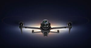 A front-facing view of a quadcopter drone, the DJI Mavic 3 Pro, with glowing lights highlighting its camera and rotors, set against a dark background.