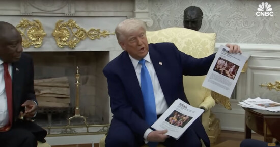 A man in a suit holds up printed documents with photos while seated in an ornate room with a fireplace; another person sits nearby. The CNBC logo is visible in the top right corner.