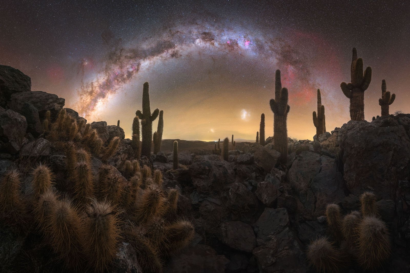 Tall cacti and rocky terrain under a night sky with the Milky Way arching brightly overhead, creating a dramatic and vibrant desert landscape.