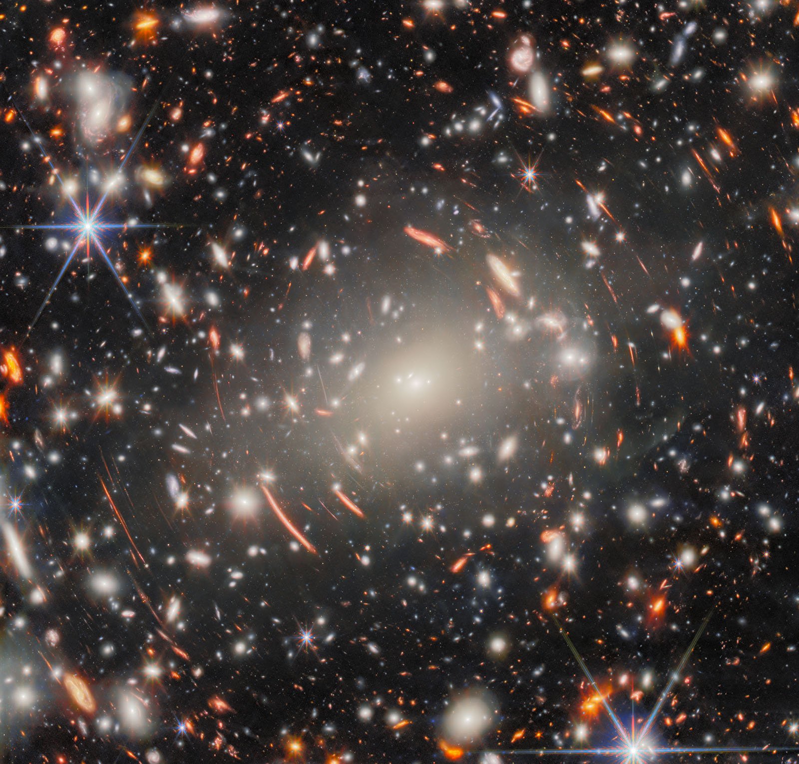 A dense field of distant galaxies, stars, and bright light distortions appear in deep space, with colorful light arcs and glowing points scattered across a dark, star-filled background.