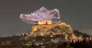 A night view of the Acropolis in Athens with colorful drone lights above it forming the shape of Aladdin’s magic lamp in the sky.