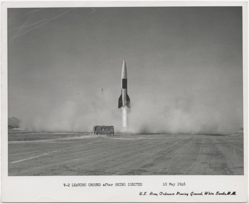 Black-and-white photo of a V-2 rocket launching, leaving the ground amid smoke and dust, taken at White Sands Proving Ground on May 10, 1946. A small structure is visible in the foreground.