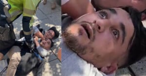 A close-up of a distressed man lying on the ground, being restrained by a uniformed officer, with another man beside him. The man's facial expression shows fear and shock.