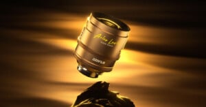 A golden camera lens with "Arles Lumière" and "DZOFILM" branding floats above a rock, illuminated by warm golden light against a dark, softly glowing background.