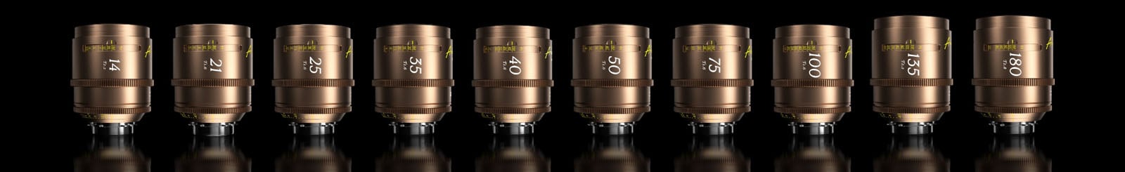 Ten gold-colored camera lenses are lined up side by side on a reflective black surface, each labeled with different focal lengths ranging from 18mm to 180mm.