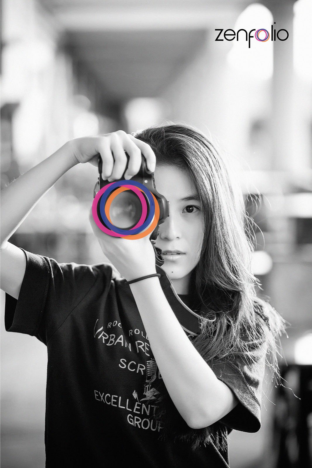 A young woman with long hair holds a camera up to her face, about to take a photo. The image is black and white except for colorful rings over the camera lens. The word "zenfolio" appears in the upper right corner.