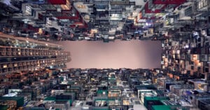 View looking up between tall, densely packed apartment buildings, creating a canyon-like effect with a narrow strip of sky visible in the center. The buildings are filled with colorful balconies and windows.