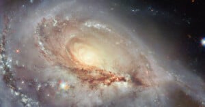 A stunning spiral galaxy with a bright, glowing center and swirling arms of stars, dust, and gas, set against a dark space background with distant star-like points of light.