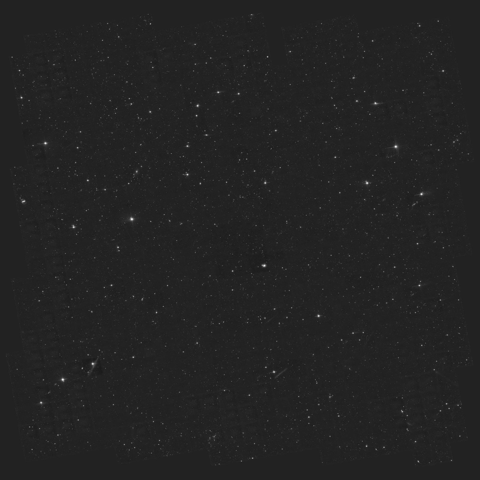 A deep space image showing a dark sky filled with numerous stars and faint galaxies scattered across the frame. Some stars appear brighter than others, creating a speckled, cosmic pattern.