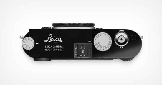 Top view of a black Leica camera, showing dials, buttons, and the lens mount; "Leica Camera New York USA" is printed on the body. The camera appears modern and sleek with a minimalist design.