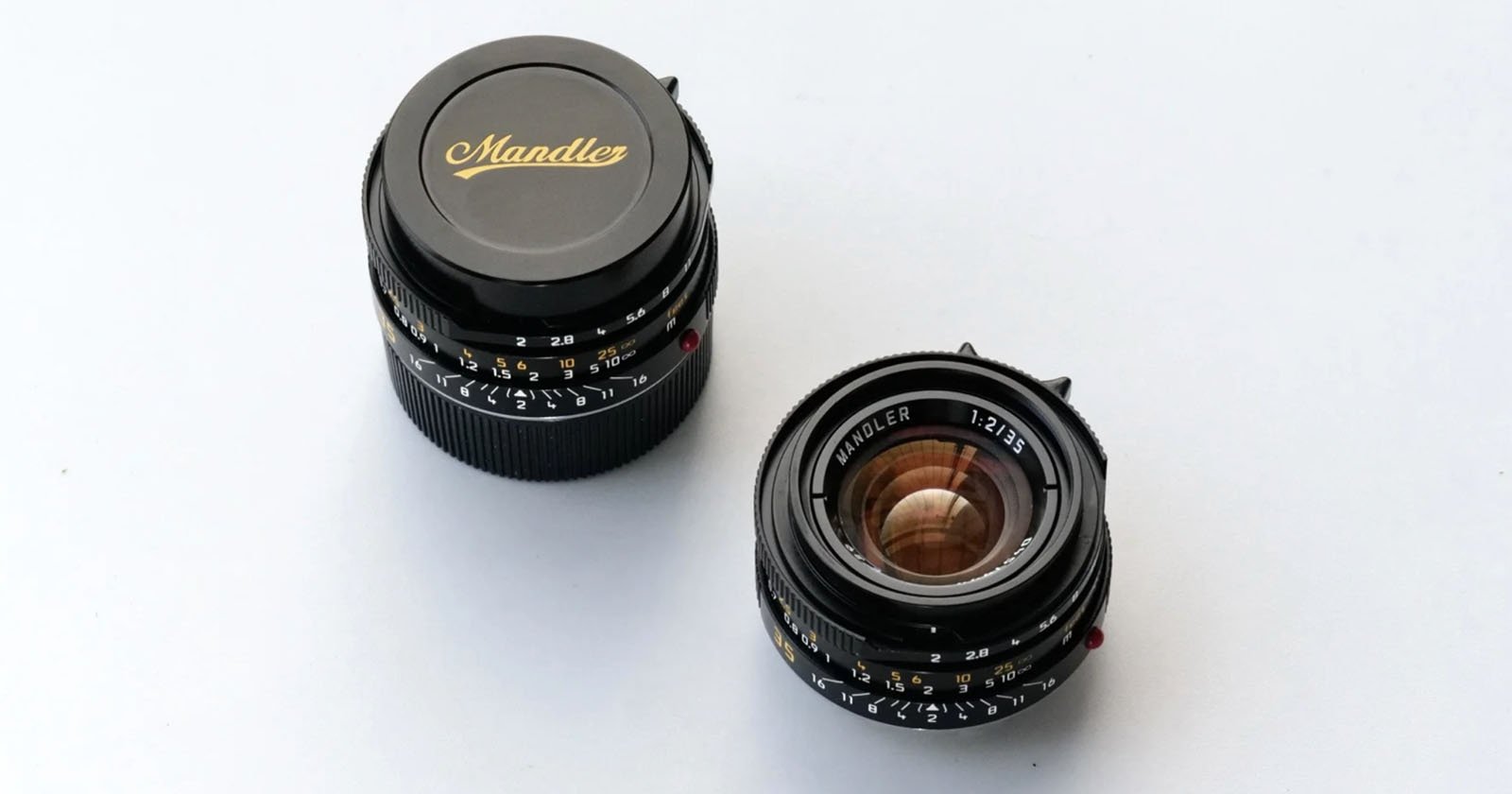 Two camera lenses are placed on a white surface; one is capped with "Mandler" written in gold script, and the other is uncapped, showing the glass and labeled "WETZLAR 1:2/35.