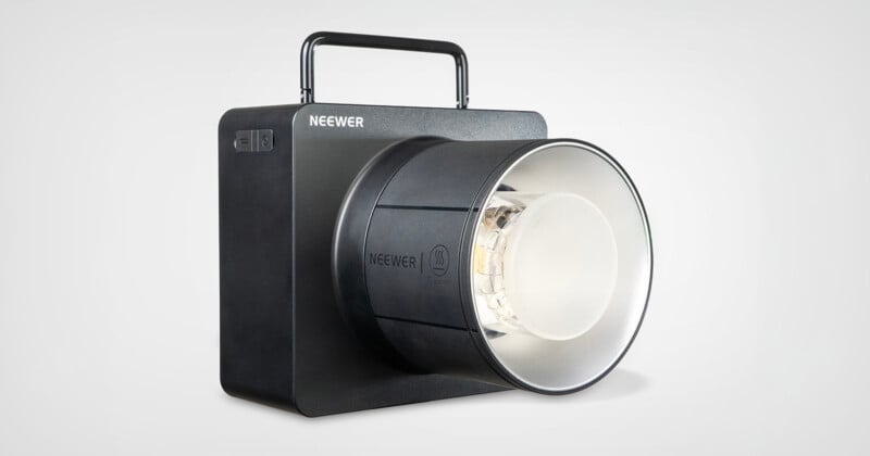 A black, box-shaped Neewer studio light with a carrying handle on top, a large round reflector at the front, and a switch on the side, set against a plain light background.