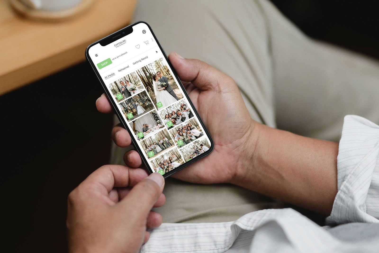 A person holds a smartphone displaying a photo gallery app with several thumbnail images of people gathered together, possibly at a party or celebration. The individual uses their thumb to scroll through the gallery.