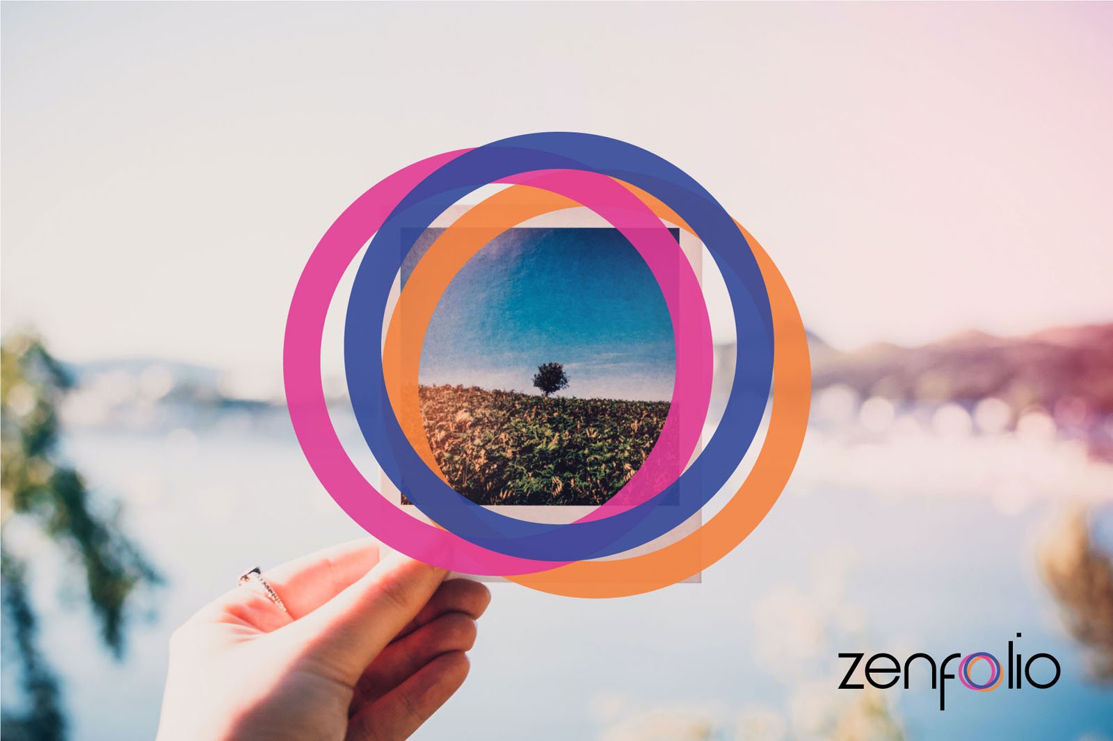 A hand holds a photo of a tree in a field, framed by overlapping blue, purple, pink, and orange circles. The blurred background shows a sunny outdoor scene. "Zenfolio" is written in the bottom right corner.