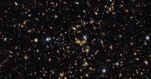 A deep space image showing countless distant galaxies, stars, and bright points of light scattered across a black background, with some stars displaying diffraction spikes.