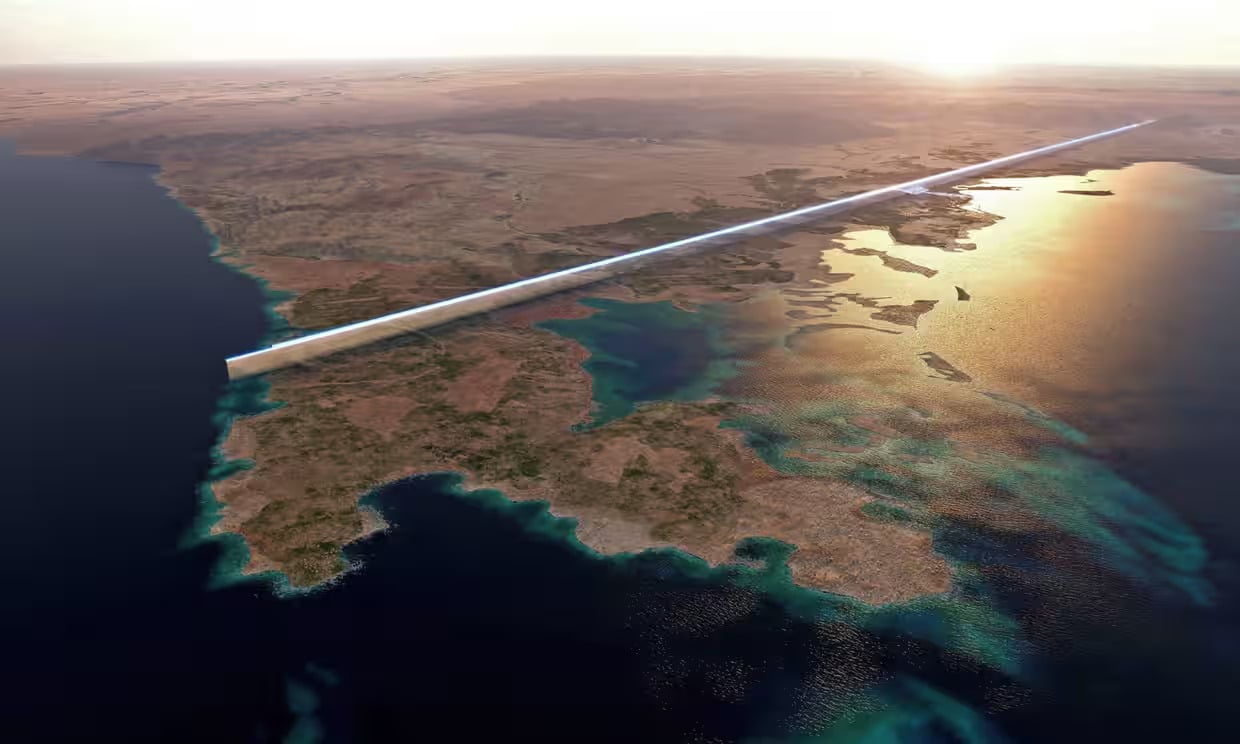 A futuristic, mirrored linear city stretches across a desert landscape beside the sea, reflecting sunlight and the coast, with water and islands in the foreground and arid terrain in the background.