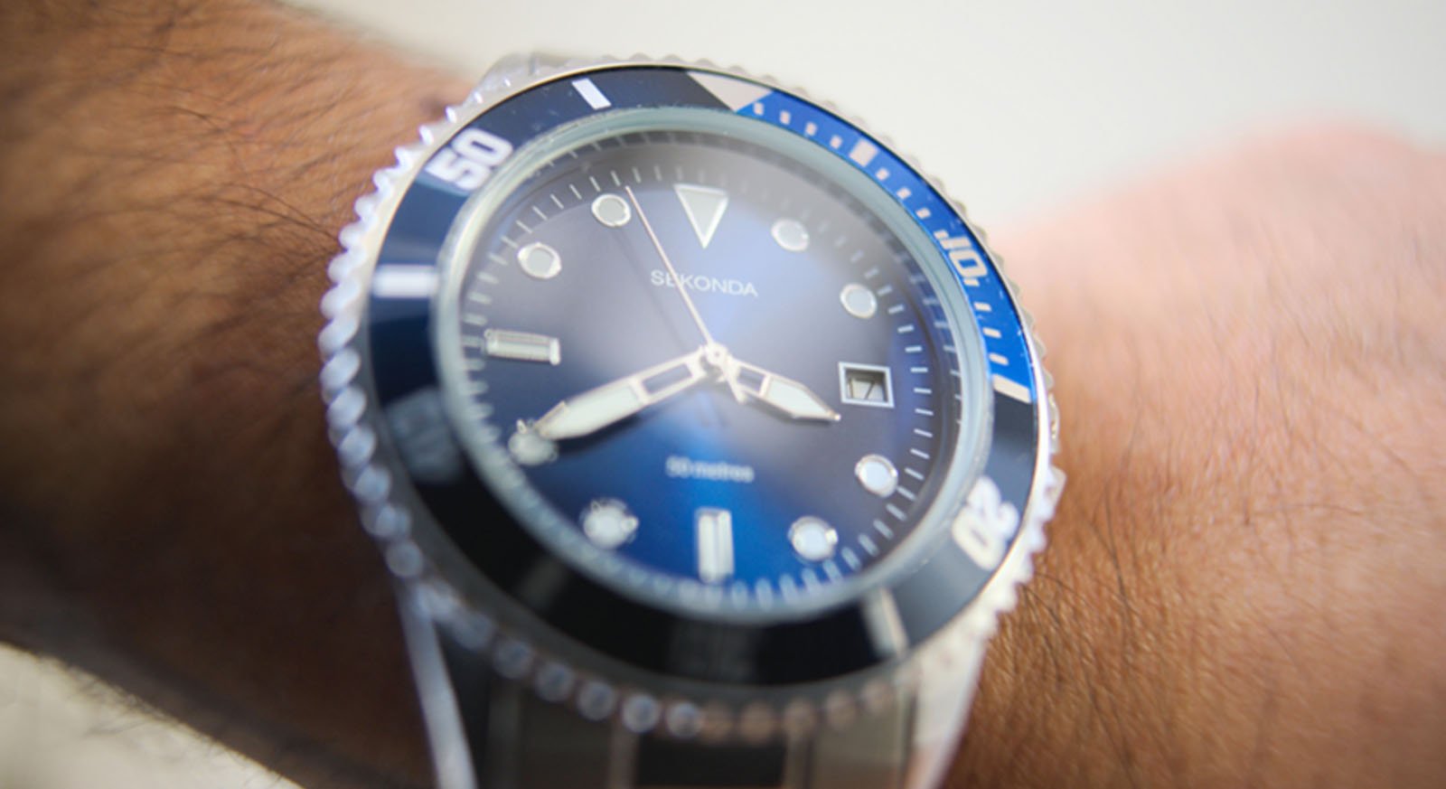 A close-up of a wristwatch with a blue and black bezel, silver hour markers, and the brand name "Sekonda" on the dial, worn on a person's wrist.