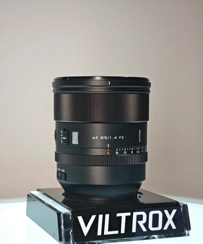 A Viltrox Pro AF 85mm f/1.4 FE camera lens is displayed upright on a black stand with the Viltrox logo, against a plain, neutral background.