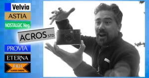 A man with a surprised expression holds a camera between his hands. On the left, there are colorful labels with names of film simulation modes: Velvia, Astia, Nostalgic Neg., Acros Std, Provia, Eterna, and Fuji Classic Chrome.
