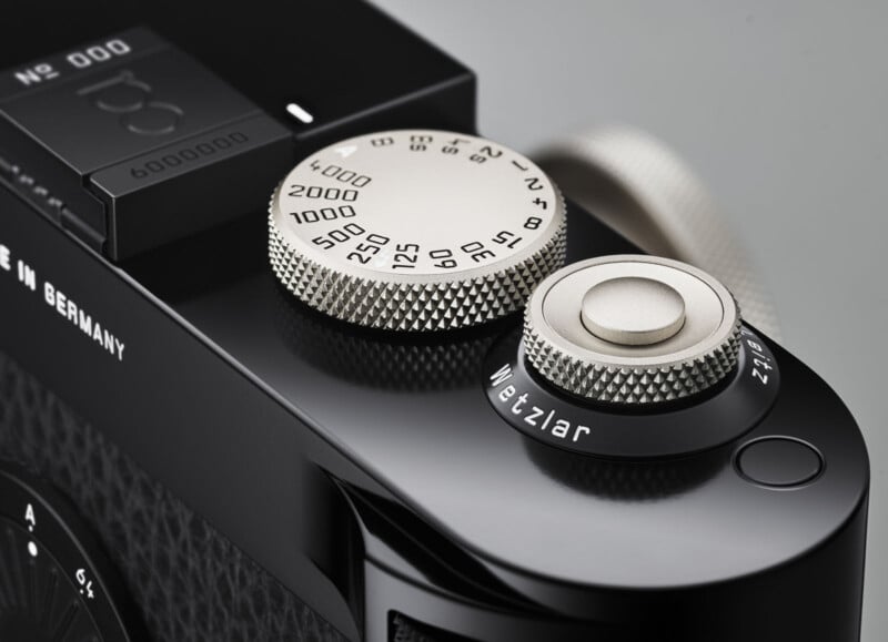 Close-up of the silver dials on a black Leica camera, showing details like shutter speed settings and the engraved word "Wetzlar" on one dial, with textured metal surfaces and part of the camera body visible.