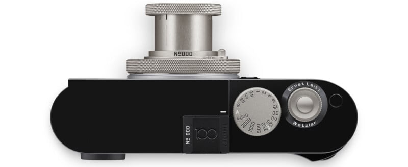 Top view of a vintage black camera with a silver lens, focusing ring, and a round dial featuring numbers and text. The camera has a sleek, minimalist design with a rectangular body.