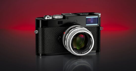 A black Leica camera with a textured grip and silver lens is displayed on a reflective surface against a gradient red and black background.