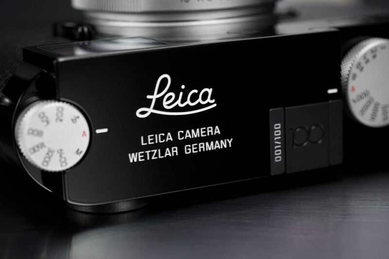 Close-up of the top plate of a Leica camera, showing the engraved Leica logo, "LEICA CAMERA WETZLAR GERMANY," and a dial with numbers, on a sleek black surface.