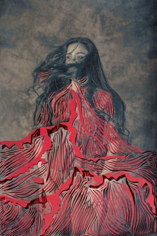 A woman with long dark hair, partially covering her face, stands against a textured background. She wears an elaborate, layered red dress with wavy, cut-out patterns resembling flowing petals or fabric.