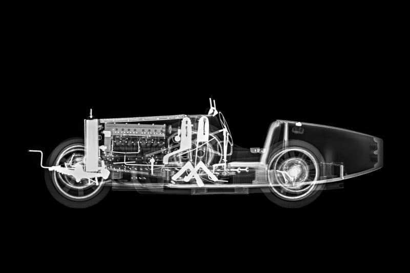 X-ray side view of a classic car revealing internal components, including the engine, seats, steering wheel, wheels, and various mechanical structures against a black background.
