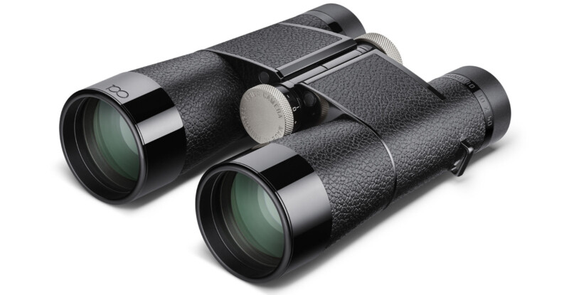 A close-up view of a pair of black binoculars with textured grips, silver adjustment dials, and green-tinted lenses facing the viewer.