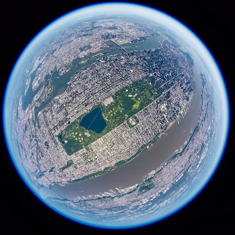 A fisheye view of Manhattan, New York City, from high above, showing Central Park as a green rectangle surrounded by dense urban areas, bordered by the Hudson and East Rivers. The Earth's curvature is visible at the edges.