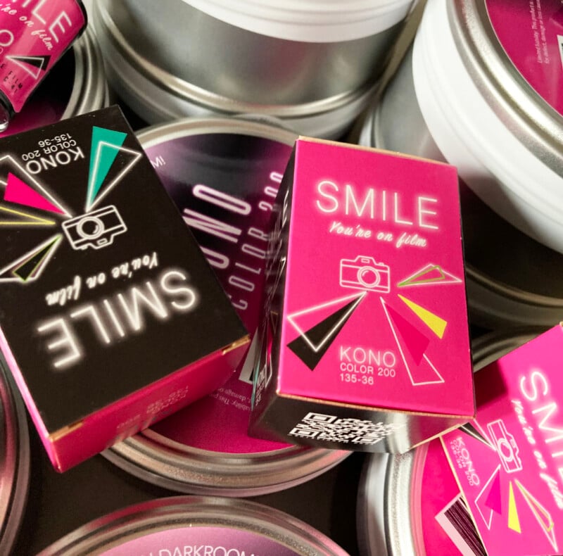A close-up of several pink and black boxes labeled "SMILE You're on film" and "KONO COLOR 200 135-36" placed among round silver tins with similar colorful labels.