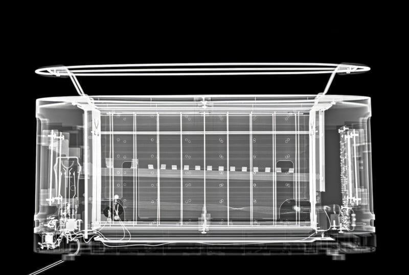 X-ray image of an electronic device showing internal components such as wires, circuits, and structural elements, all visible in high contrast on a black background.