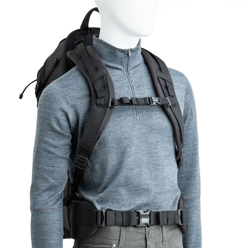 A mannequin wearing a gray long-sleeve zip-neck shirt and a large black backpack with padded shoulder straps, chest strap, and waist belt, against a white background.