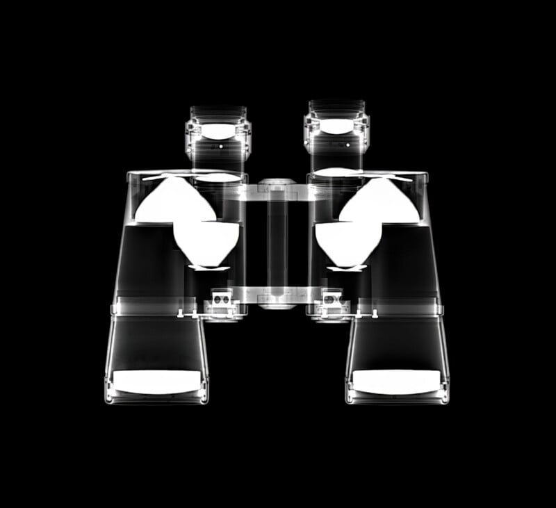 X-ray image of a pair of binoculars on a black background, revealing the internal lenses and mechanical components in a symmetrical, transparent view.