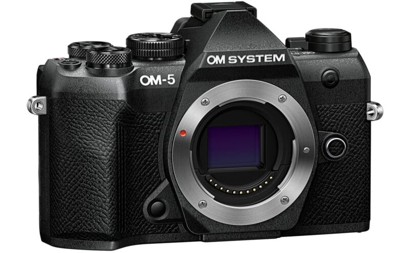 A black OM System OM-5 mirrorless digital camera body with textured grip and visible lens mount, viewed from the front-left angle. No lens is attached.