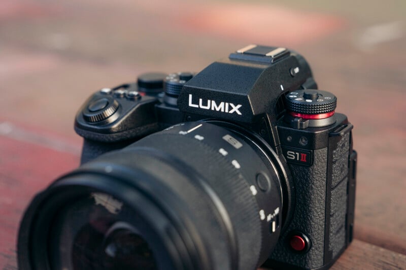 Close-up of a black Panasonic Lumix S1 II digital camera with a large lens, placed on a wooden surface. The camera's brand name and controls are clearly visible.