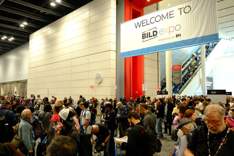Large crowd of people gather inside a convention center under a sign reading "Welcome to BILD expo." People are waiting, talking, and moving toward escalators in a busy, well-lit space.