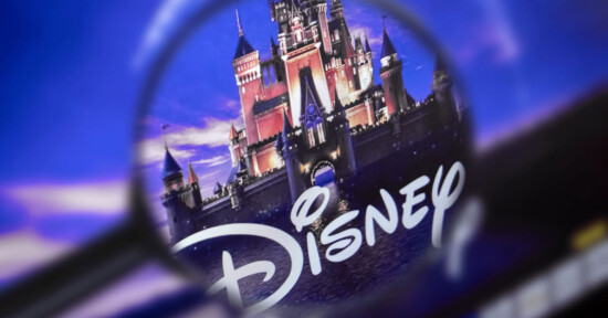 A magnifying glass focuses on the Disney logo in front of a castle, with a purple and blue background, highlighting the castle's details and the stylized "Disney" text.
